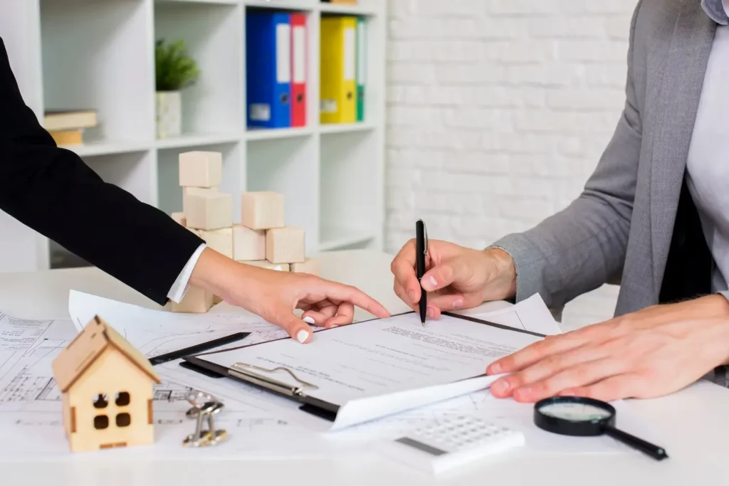 Hands of a lawyer and client reviewing lease documents on a table, with a wooden house model and building blocks in the background, symbolizing tenant rights and legal assistance in Addison, Texas.