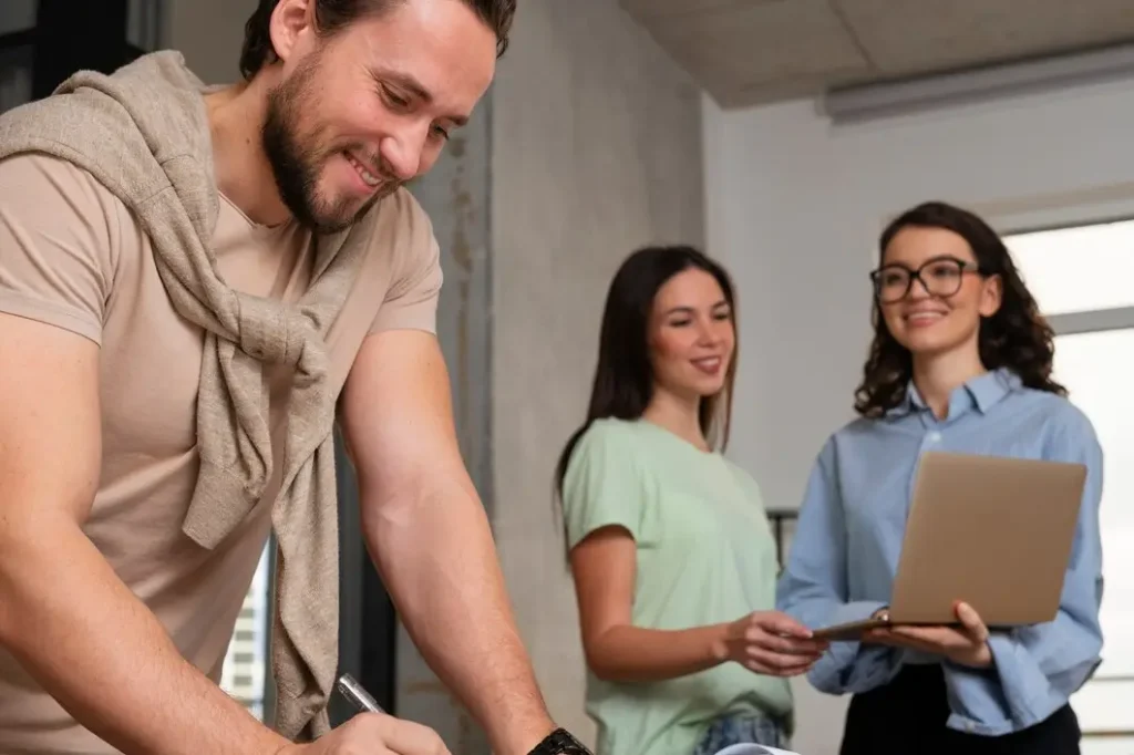 Group of three people collaborating in a modern office setting, with a man writing notes and two women discussing information on a laptop, reflecting tenant advocacy and legal support in Central East Austin.