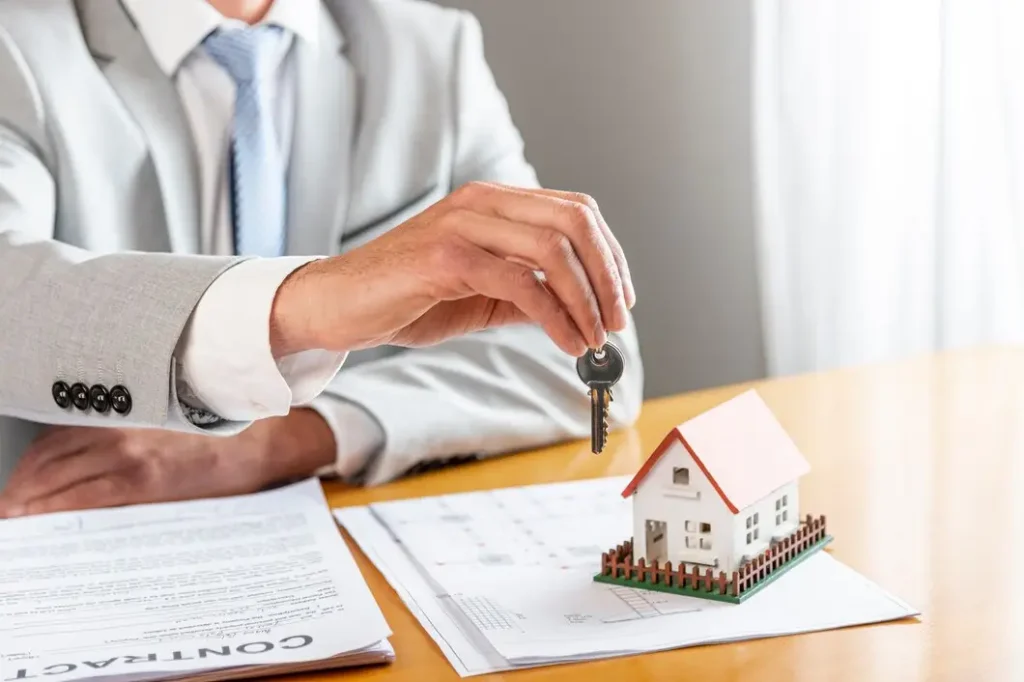 Hand of a lawyer holding a key above a miniature house model, with rental agreements and contracts on a table, symbolizing tenant rights and legal services in Dell Parmer South Campus.
