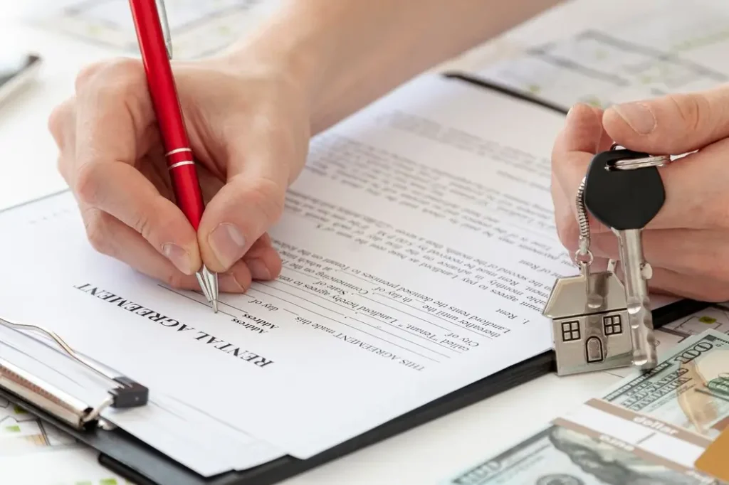 Hand holding a red pen signing a rental agreement, with house-shaped keychain and cash visible, illustrating tenant rights and lease negotiations in East Cesar Chavez.