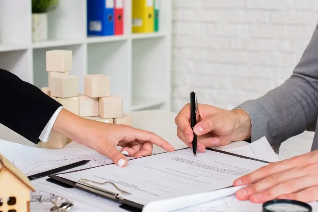 Hands reviewing lease documents on a table, with a house model and building blocks in the background, representing landlord-tenant legal services in Frisco, Texas.