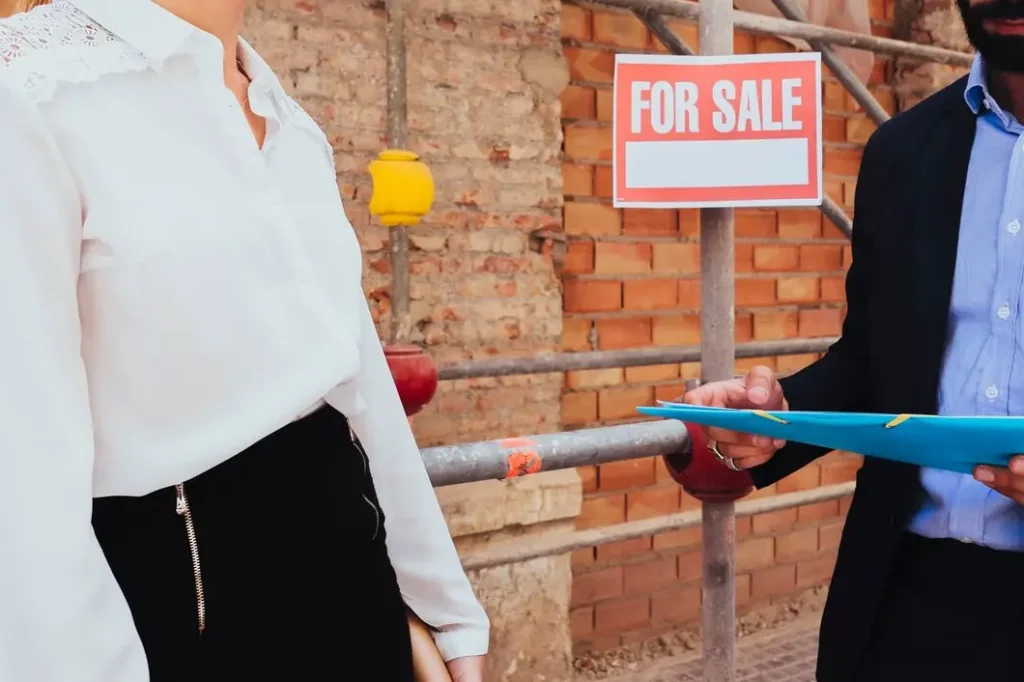 Person discussing property with a clipboard in front of a "FOR SALE" sign, representing tenant rights and housing issues in Greater South River City.
