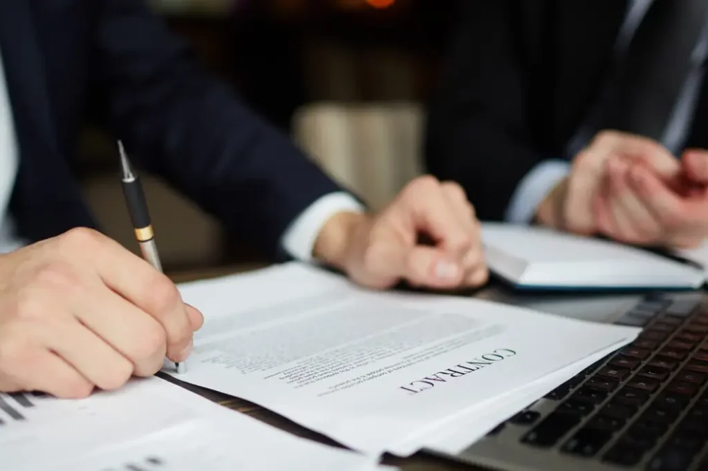 Hands signing a contract document with the word "CONTRACT" visible, alongside a laptop and another person in a business setting, representing legal consultations for landlord-tenant issues in Kaufman County, Texas.