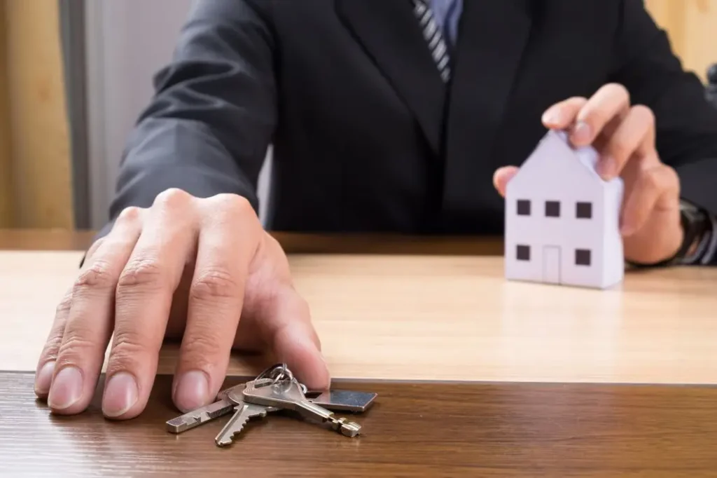 Man in a suit placing keys on a table, with a small model house in the background, symbolizing tenant rights and legal support in housing matters.