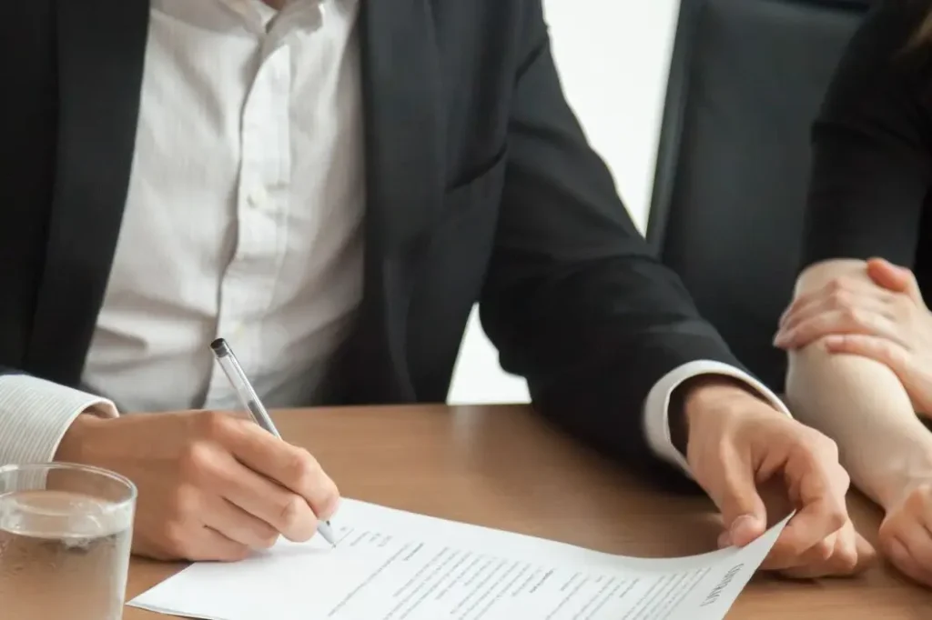 Person in a suit signing a lease agreement with a pen, glass of water on the table, illustrating legal consultation for landlord-tenant issues.