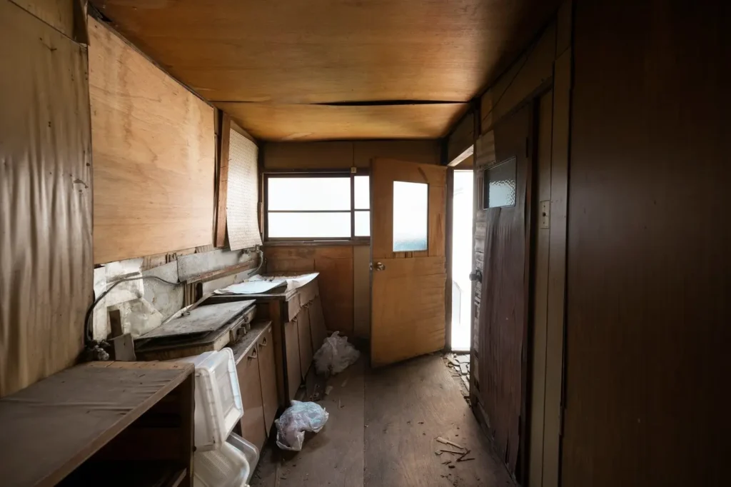 Interior of a neglected and dilapidated kitchen with wooden cabinetry, visible debris, and an open door leading outside, illustrating potential housing issues relevant to tenant rights and safety in South Lamar.