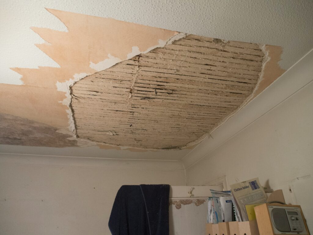 Damaged ceiling with peeling wallpaper and exposed structure, highlighting unaddressed repair issues in a rental home.
