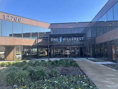 Office building exterior of One Hillcrest, featuring the address 12700 and landscaped entrance with flowers, located in Dallas, Texas, near the Law Office of Bryan Fagan PLLC.