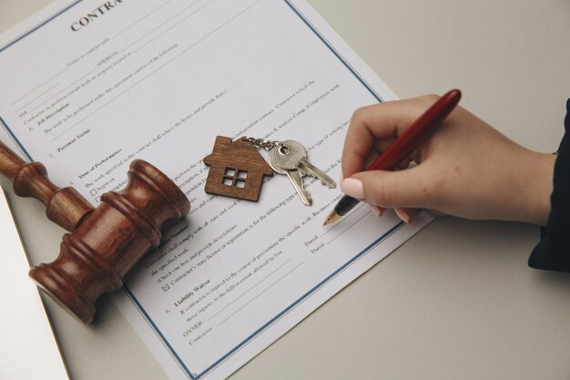 Hand holding a pen signing a lease agreement, with a gavel and house keys on the table, symbolizing tenant rights and legal representation in West University, Texas.