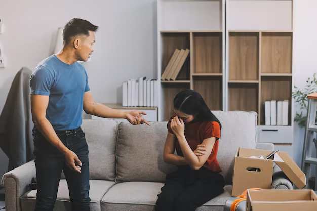 Man arguing with a woman sitting on a couch, showing emotional distress, surrounded by moving boxes, illustrating tenant disputes and landlord harassment issues.