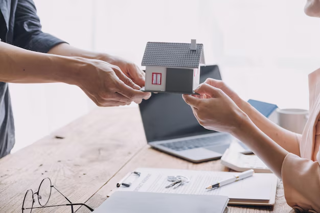 Hands exchanging a miniature house model over a wooden table, symbolizing tenant rights and property leasing discussions, with a laptop and documents in the background.