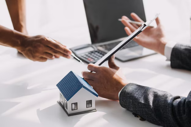 Hands exchanging a document with a miniature house model on the table, symbolizing tenant law services and lease negotiations in a professional setting.