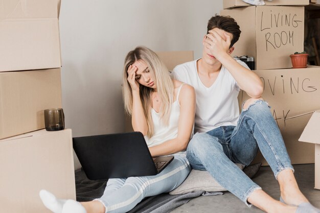 Upset couple sitting on the floor surrounded by moving boxes, looking stressed while using a laptop, symbolizing tenant struggles and lease disputes in Bulverde.