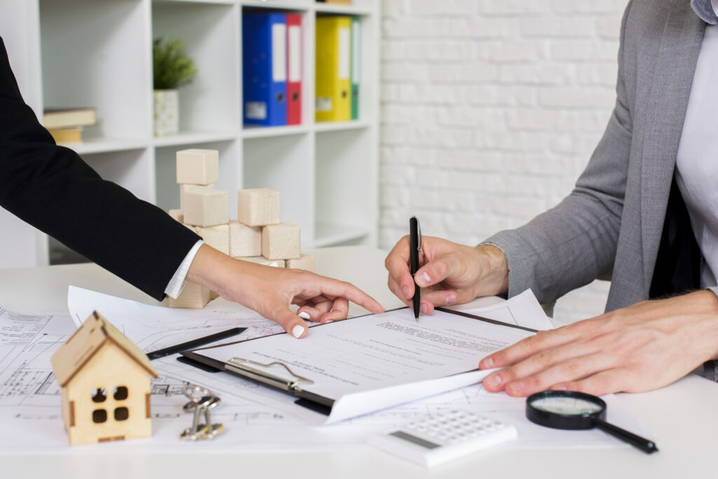 Hands discussing lease agreements with a wooden house model and building blocks on a table, emphasizing tenant rights and legal consultation.