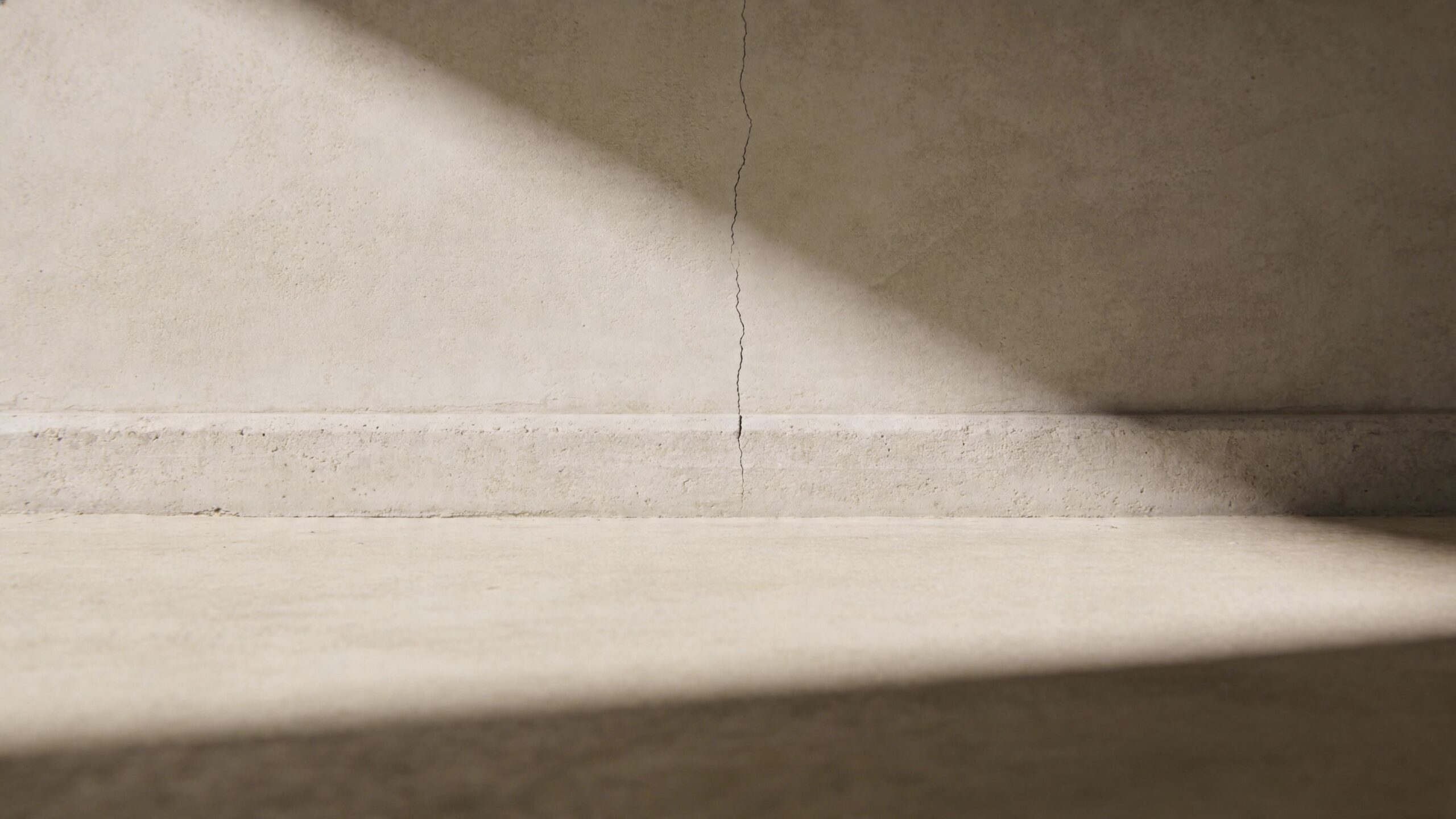 A close-up view of a vertical crack running through a plain concrete wall and baseboard.