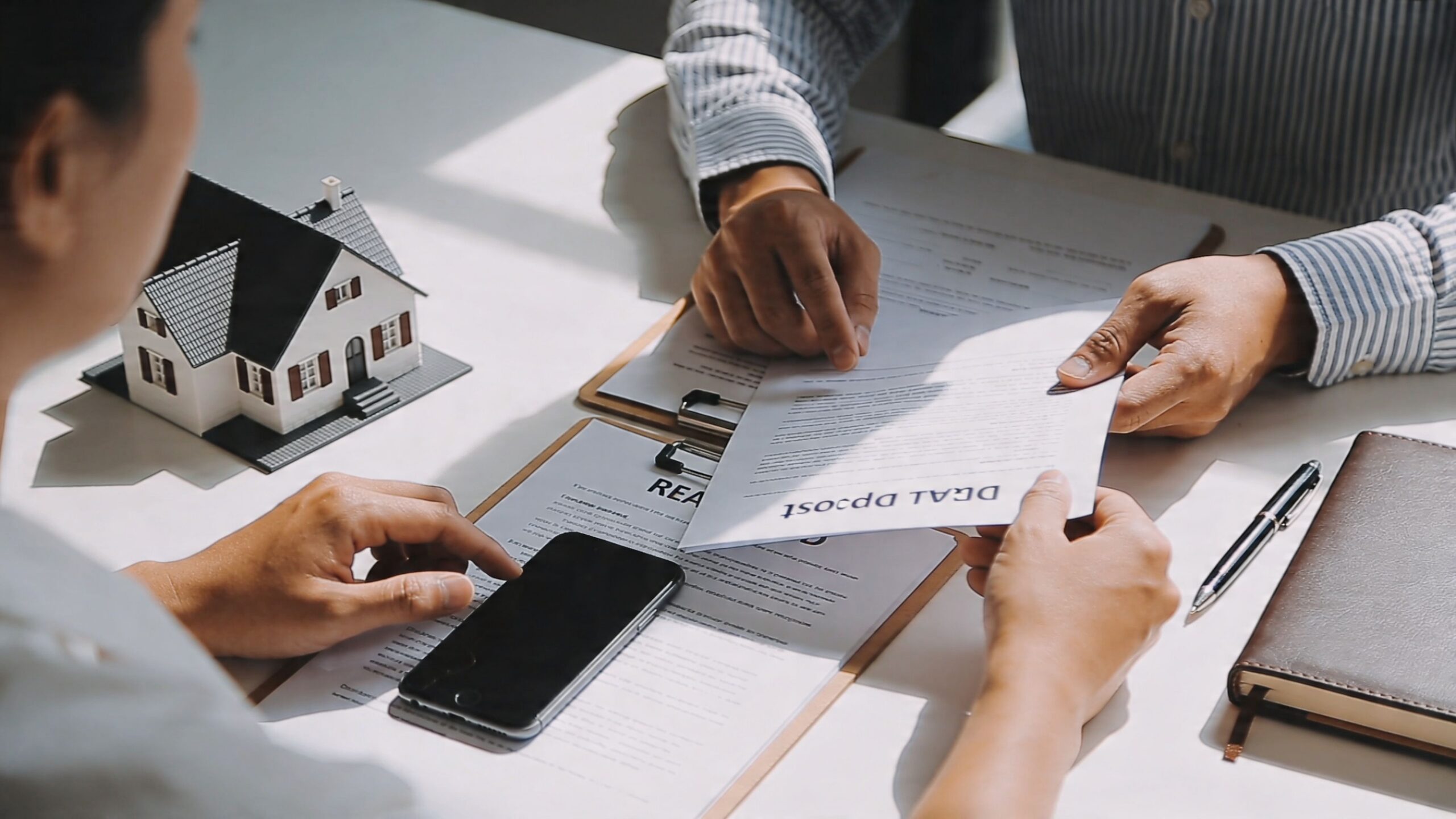 A real estate agent reviews a rental deposit document with a client next to a model house.